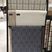 A display rack holding several carpet samples of varying textures and patterns in shades of gray, beige, and dark blue.