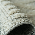 A close-up view of a rolled, textured beige and grey area rug showing the layered pile and woven fabric backing.