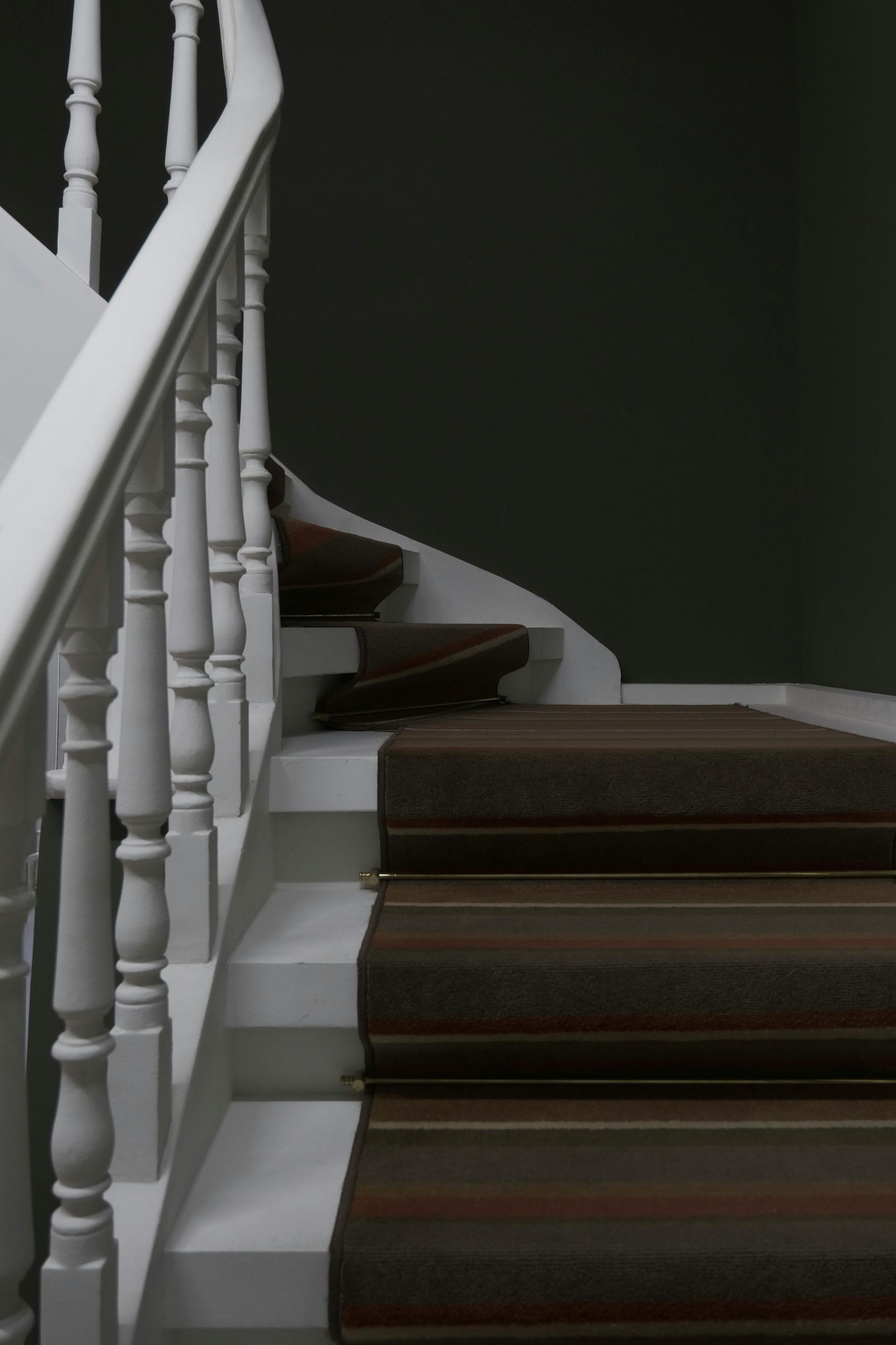 Staircase with white railings and brown carpeted steps leading upward against a dark wall.