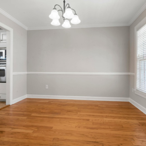 A red and black vacuum cleaner head moves across hardwood flooring next to a patterned rug.