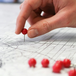 A hand placing a red pushpin on a detailed paper map.