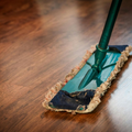 A green mop with a worn, frayed cloth head resting on a polished dark wood floor.
