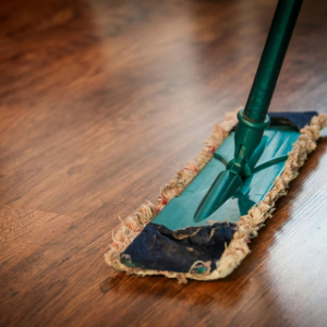 A green mop with a worn, frayed cloth head resting on a polished dark wood floor.