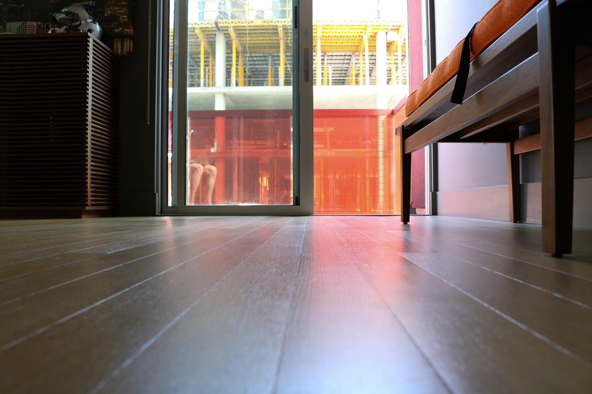 Low-angle view of a room with wooden floor, table and bench, facing an open door to a red patio.