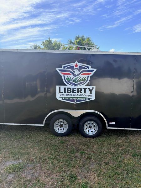Black Liberty University trailer with logo parked on grass under a blue sky.