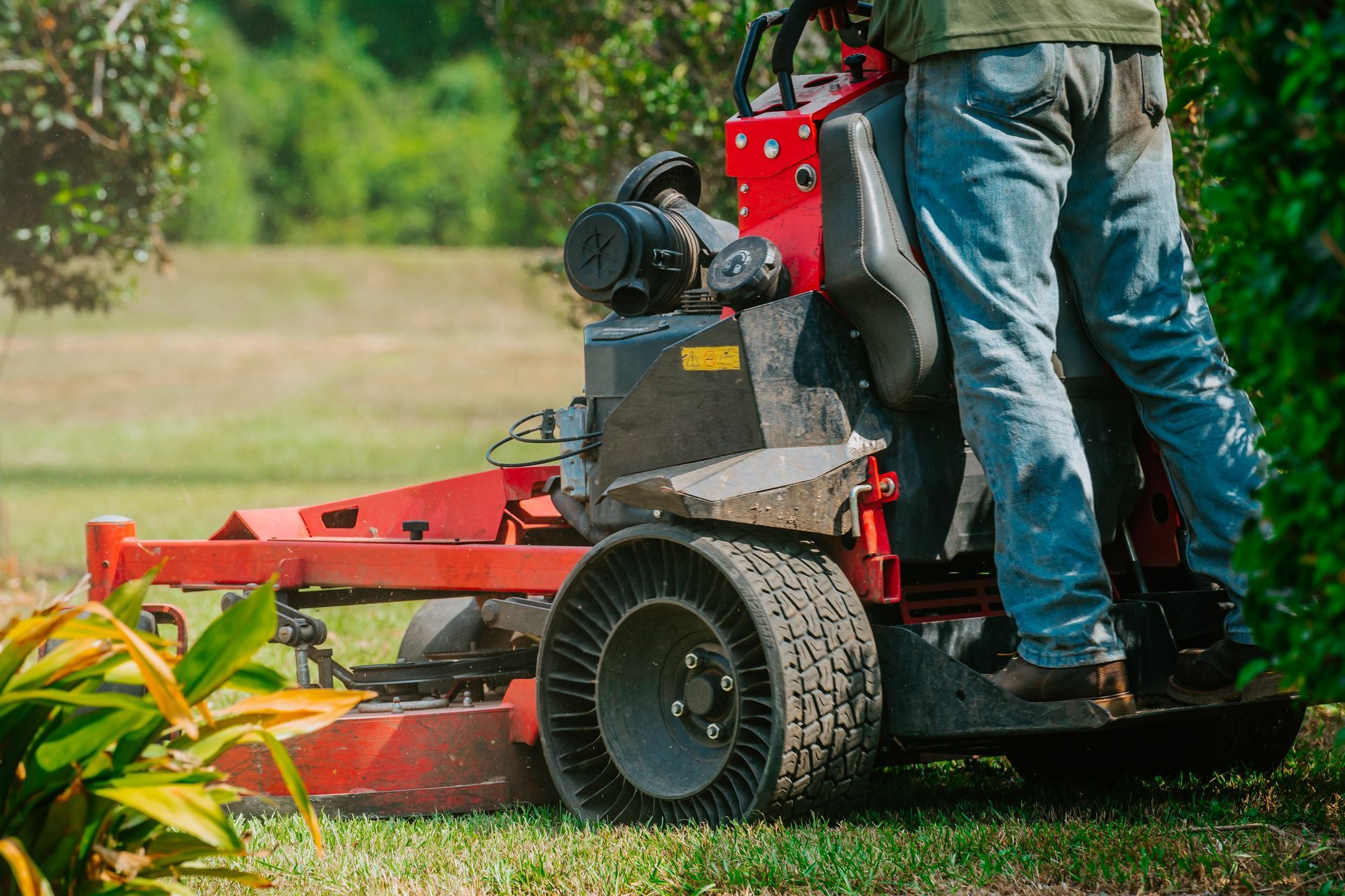 Person using a red riding lawn mower on grass outdoors