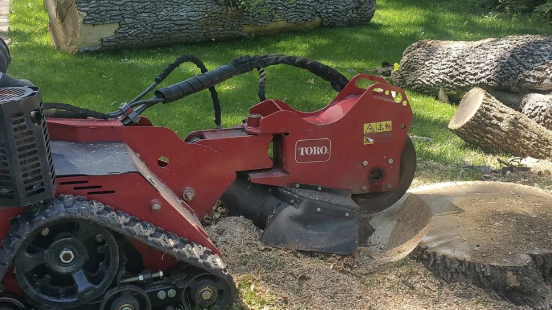 A red tractor is cutting a tree stump in the grass.
