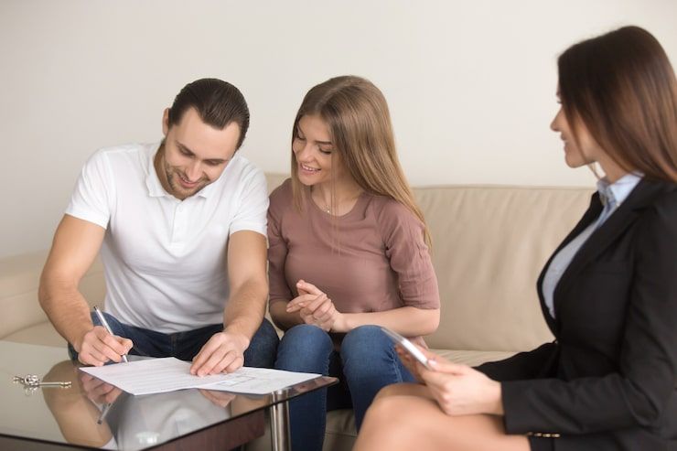 Three people discussing paperwork at a table, with one man signing a document.