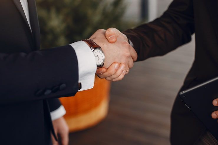 Two people in suits shaking hands, close-up with a watch visible on one wrist.