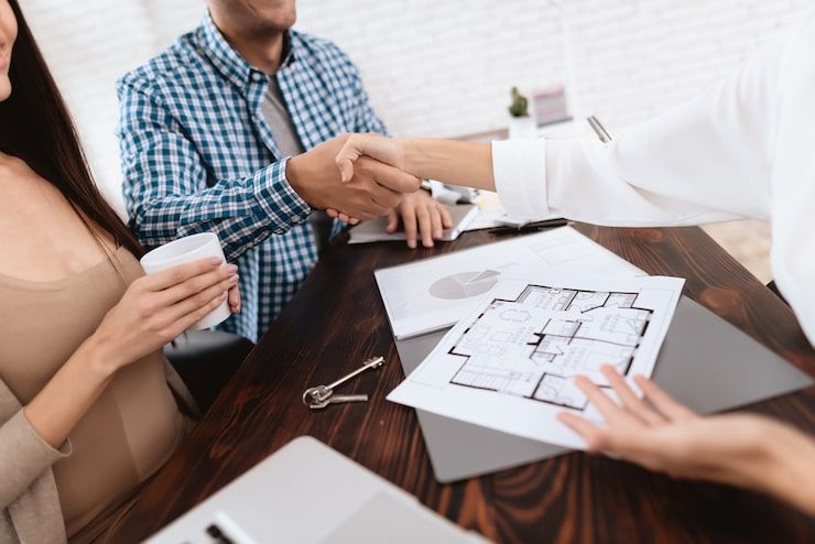 People shaking hands over a floor plan on a desk during a real estate meeting