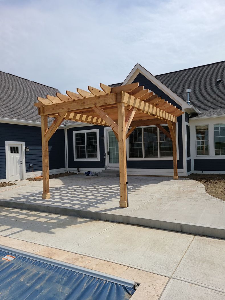 Wooden pergola beside a pool in a backyard patio with a dark-sided house behind it