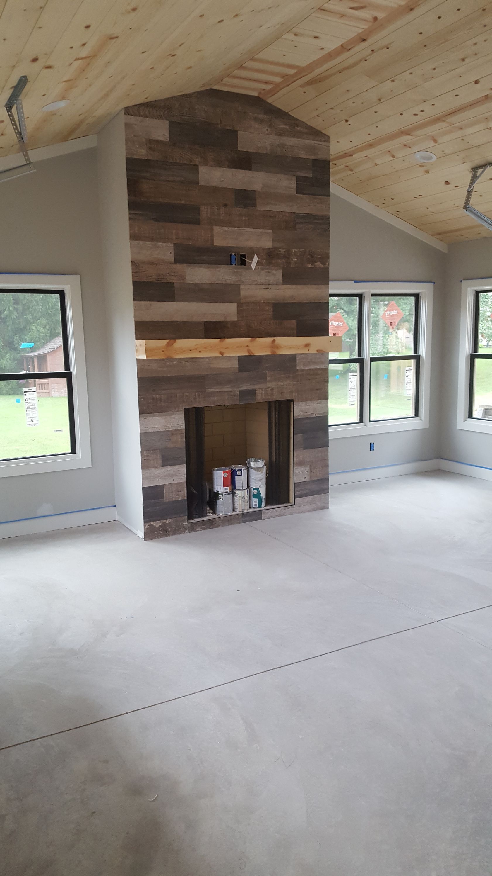 Empty room with sloped wood ceiling, large stone fireplace, and windows on both sides