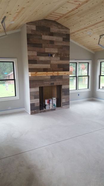 Unfinished room with a wood-clad fireplace wall and large windows under a vaulted ceiling.