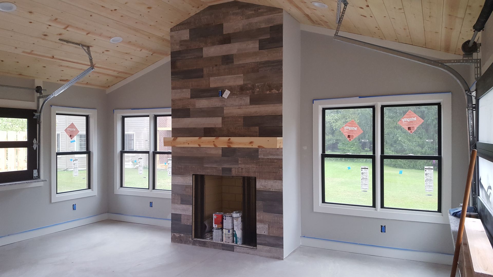 Bright living room with vaulted wood ceiling, stone fireplace, and multiple windows overlooking grass.