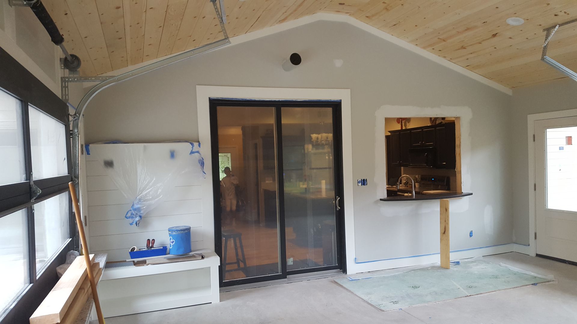 Interior of a partially finished room with a glass door, white wall, and built-in fireplace under a wood ceiling.