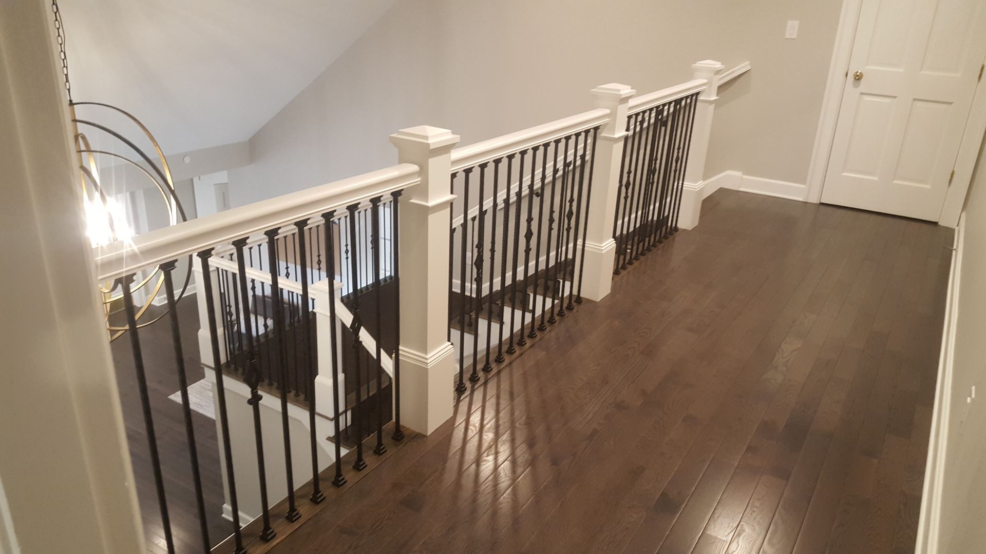 Stair landing with dark wood floor and white railing overlooking a staircase and hallway doors
