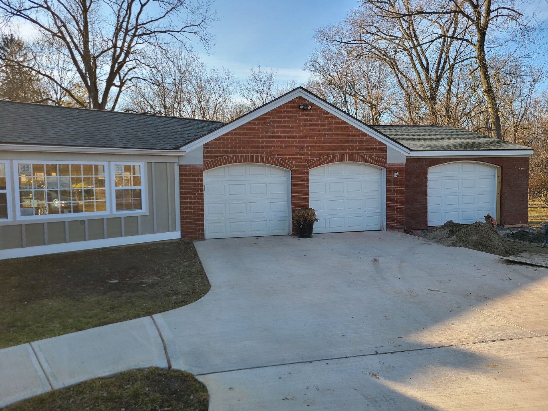Suburban brick garage with three white doors and a wide concrete driveway at dusk