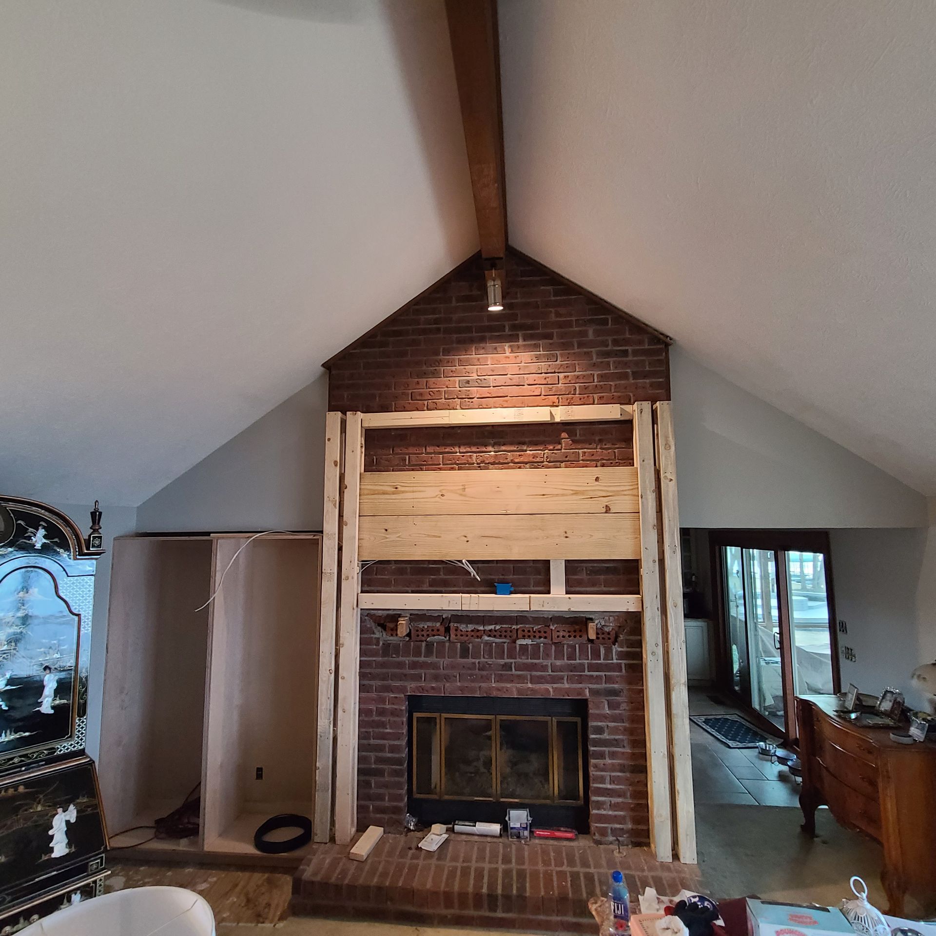 Attic living room with a brick fireplace, vaulted ceiling, and unfinished walls under renovation