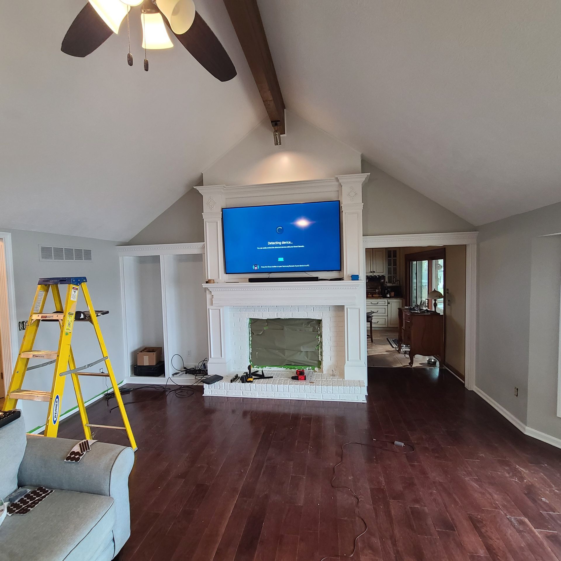 Living room with vaulted ceiling, white fireplace and TV, dark hardwood floors, and a yellow ladder.