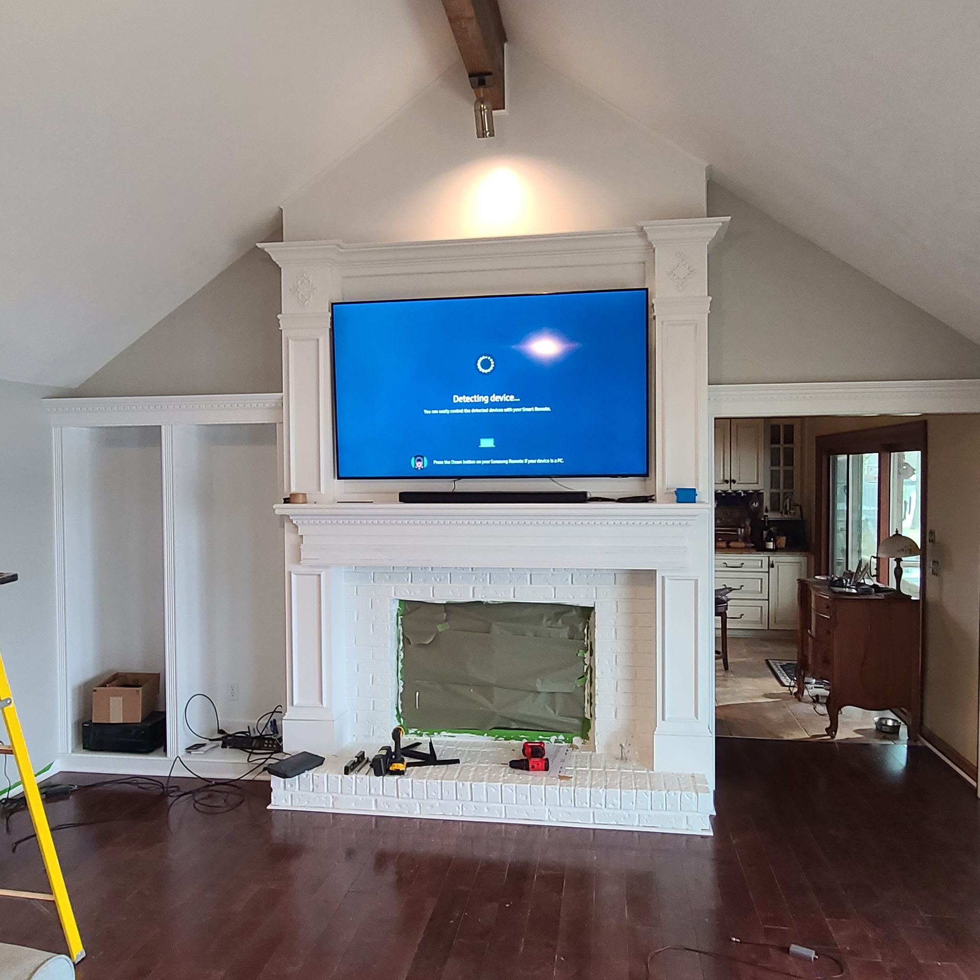 Living room with a white fireplace, wall-mounted TV, and dark hardwood floors under a vaulted ceiling