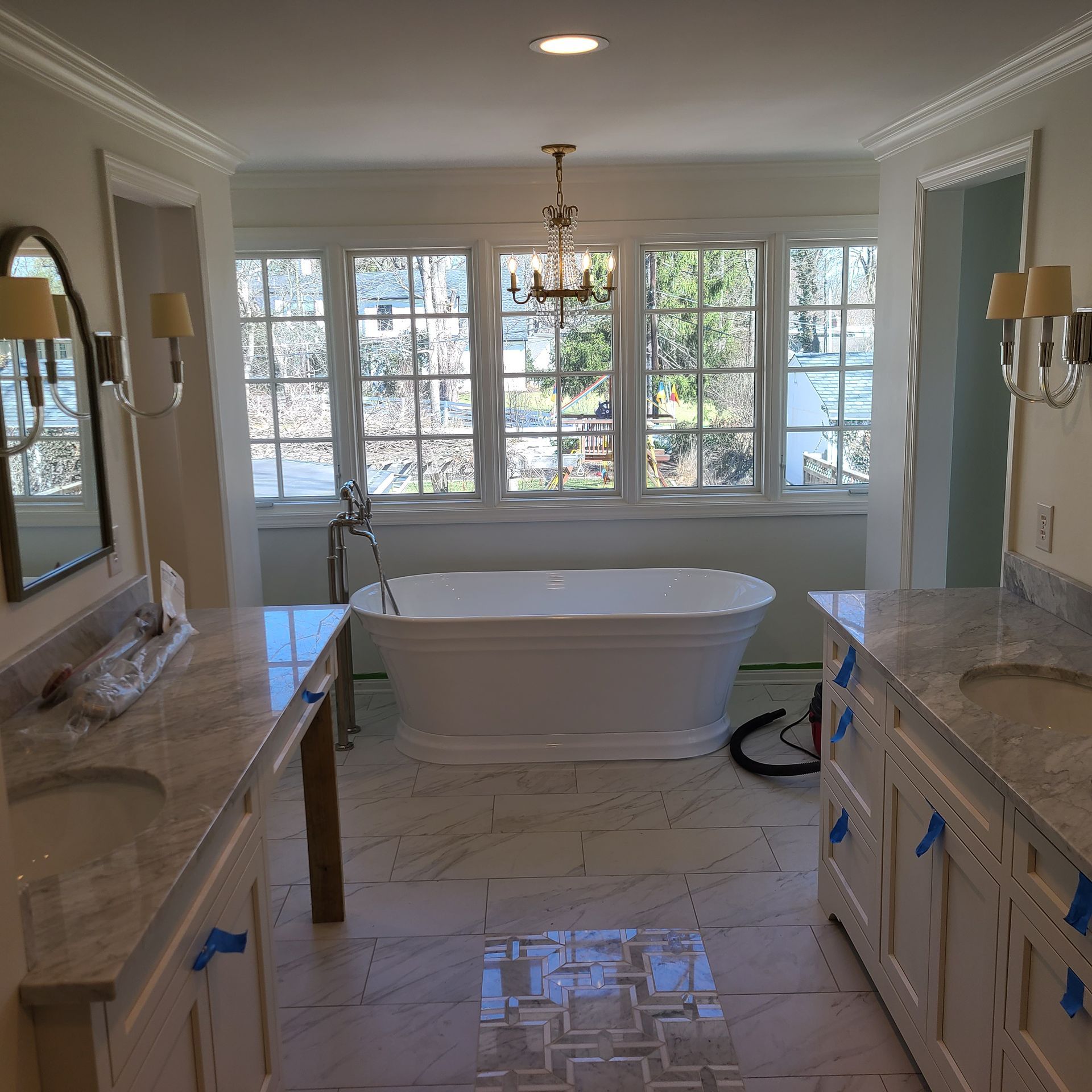 Bright bathroom with a freestanding tub, marble vanities, and large windows overlooking trees.