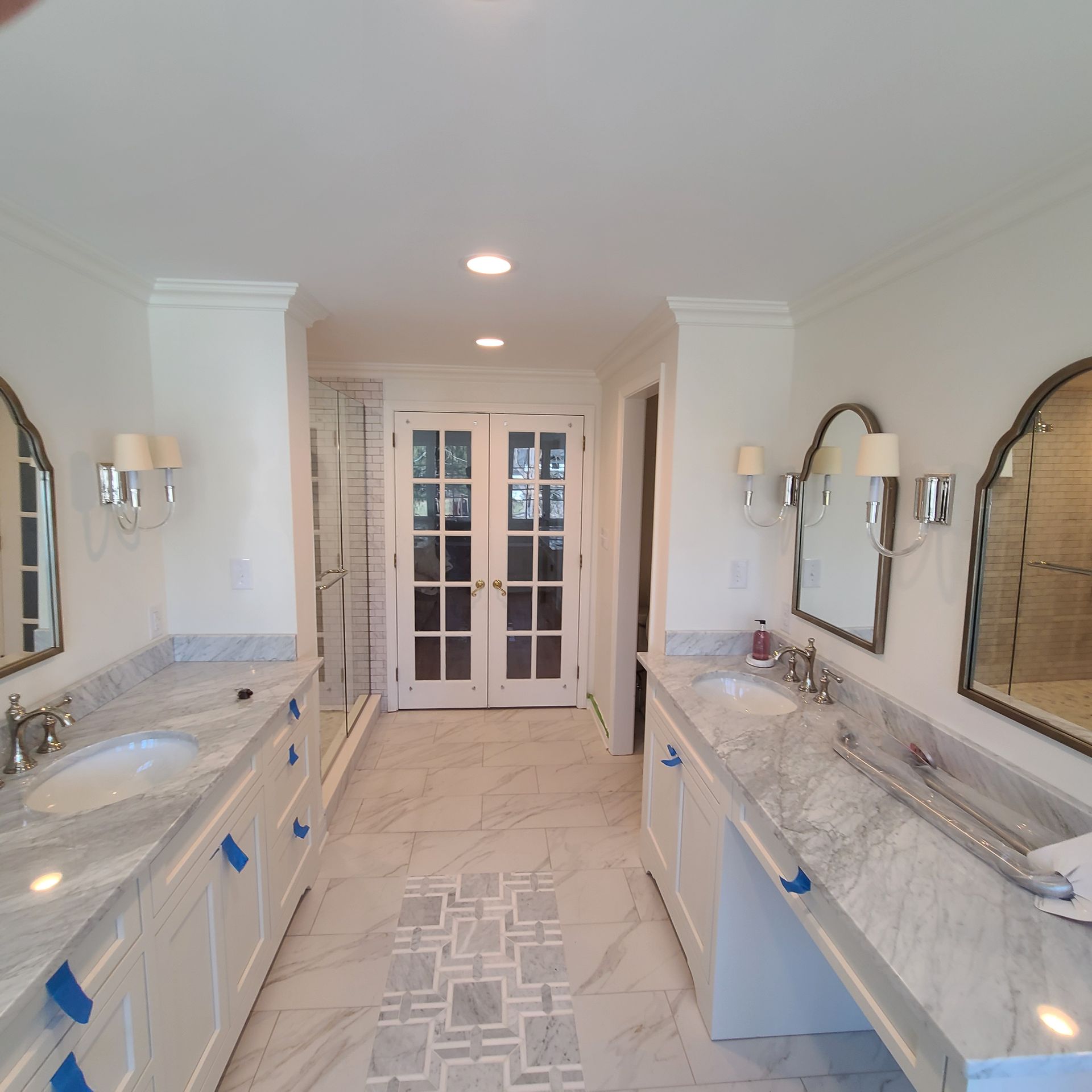 Elegant double vanity bathroom with marble counters, arched mirrors, and French doors at the far end