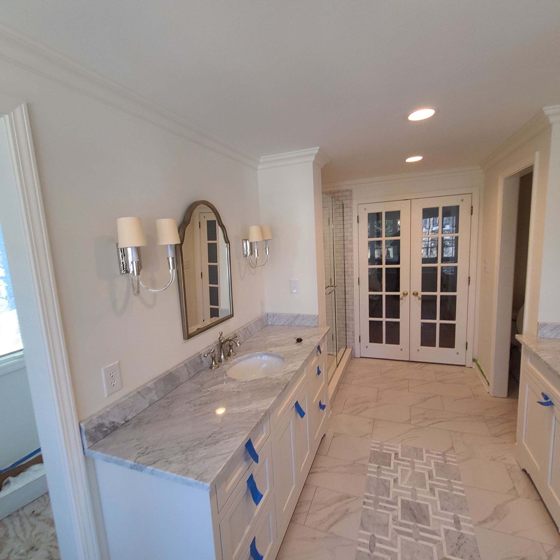 Elegant bathroom with marble double vanity, wall sconces, mirror, and French doors leading out.