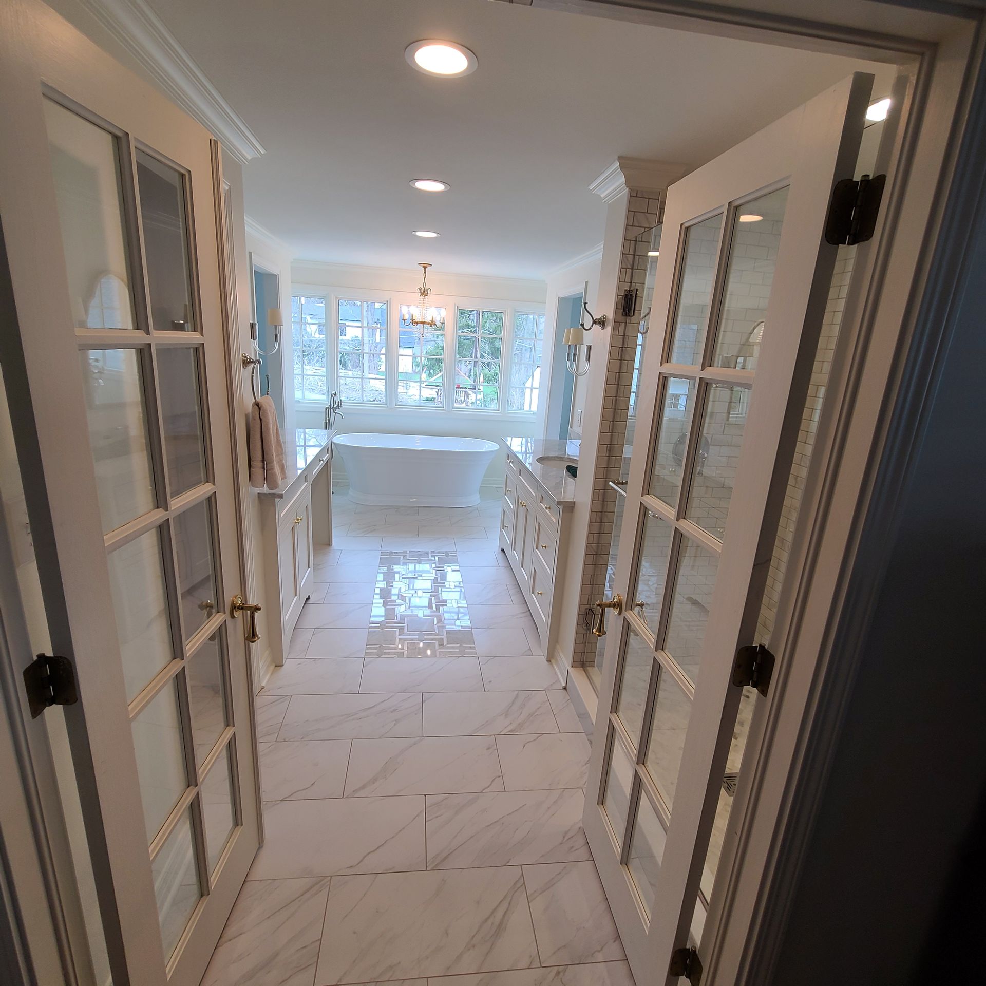 Bright hallway with French doors opening to a sunlit room and large windows at the end.