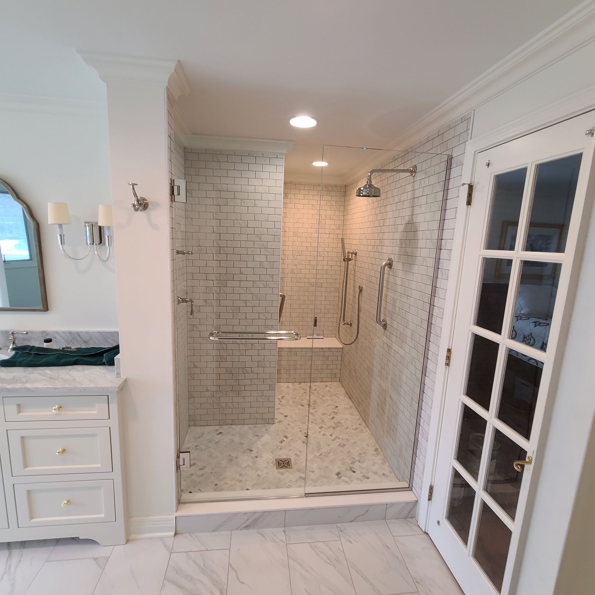 Luxury bathroom with white tiled walk-in shower, glass door, and marble vanity cabinet