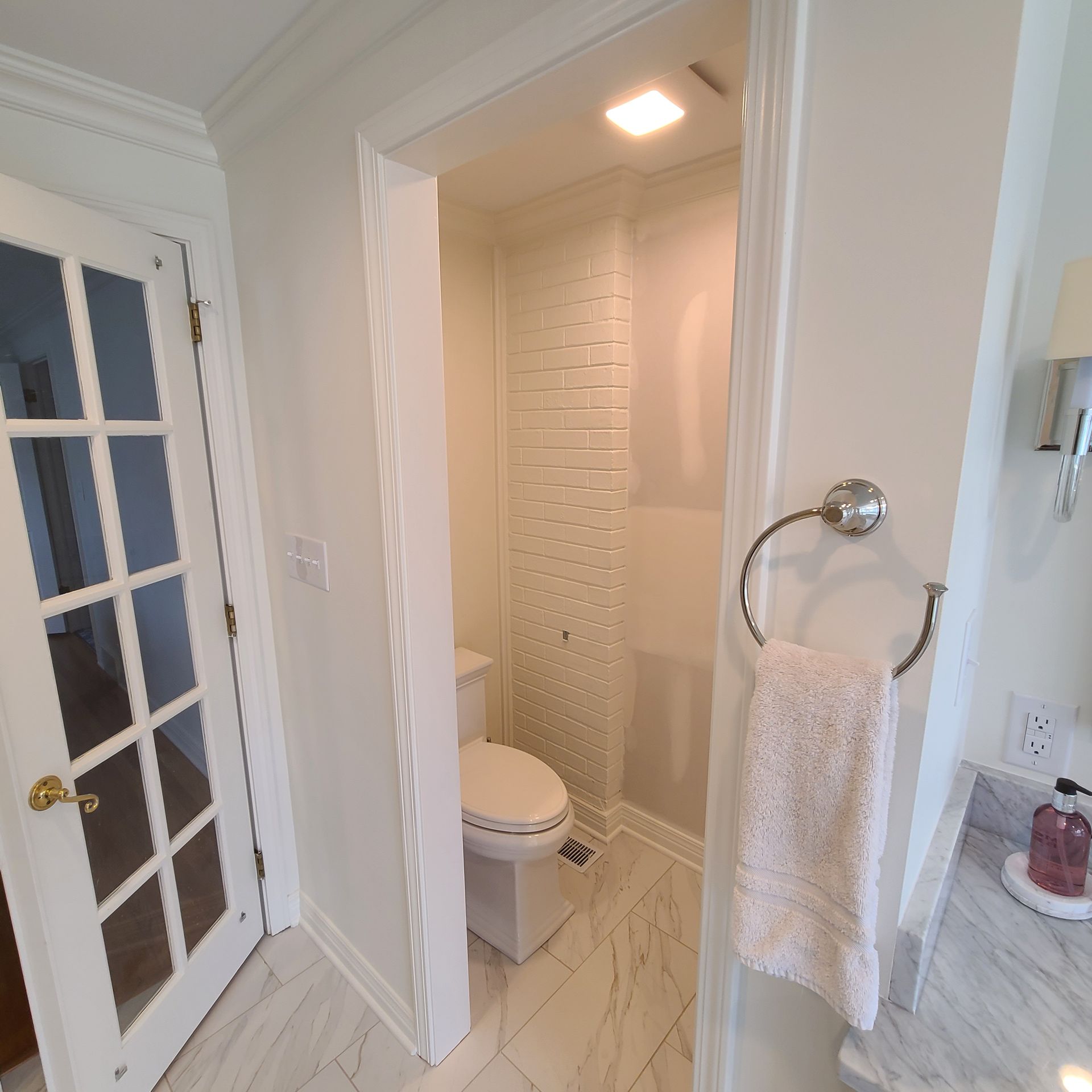 Bathroom doorway with a toilet, glass shower, towel ring, and vanity countertop in a bright white interior