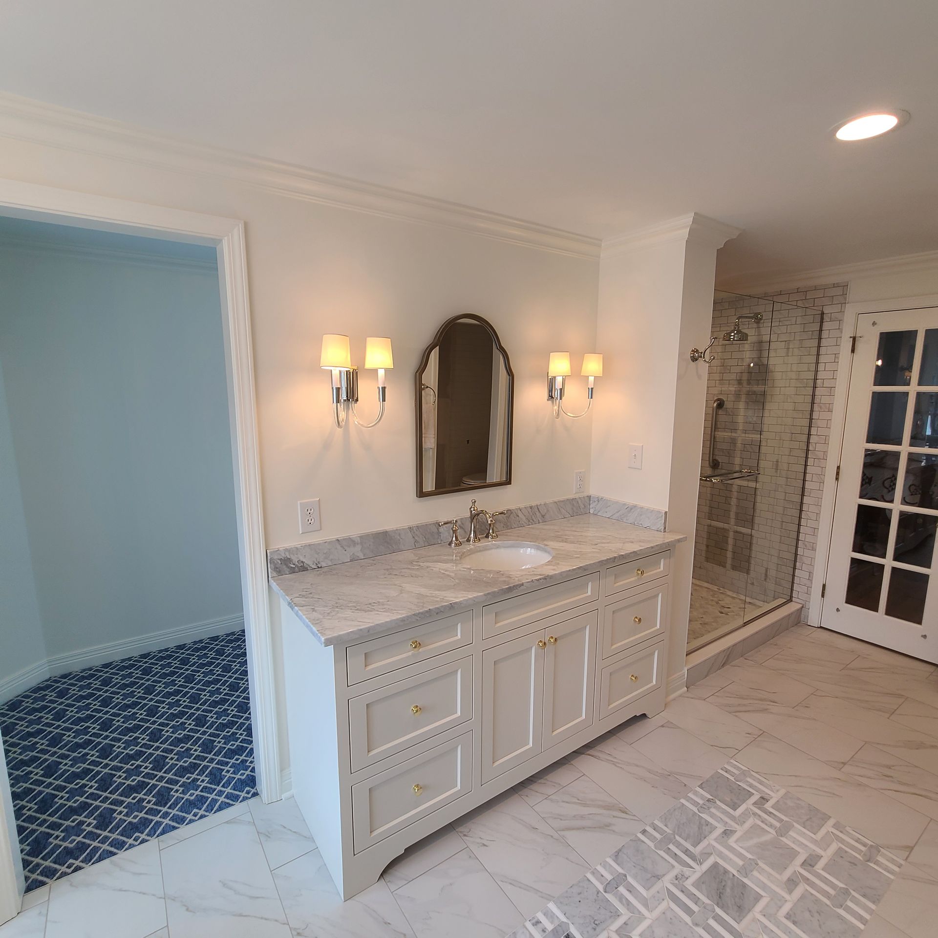 Elegant bathroom with double vanity, mirror sconces, tiled shower, and patterned floor in soft neutral tones