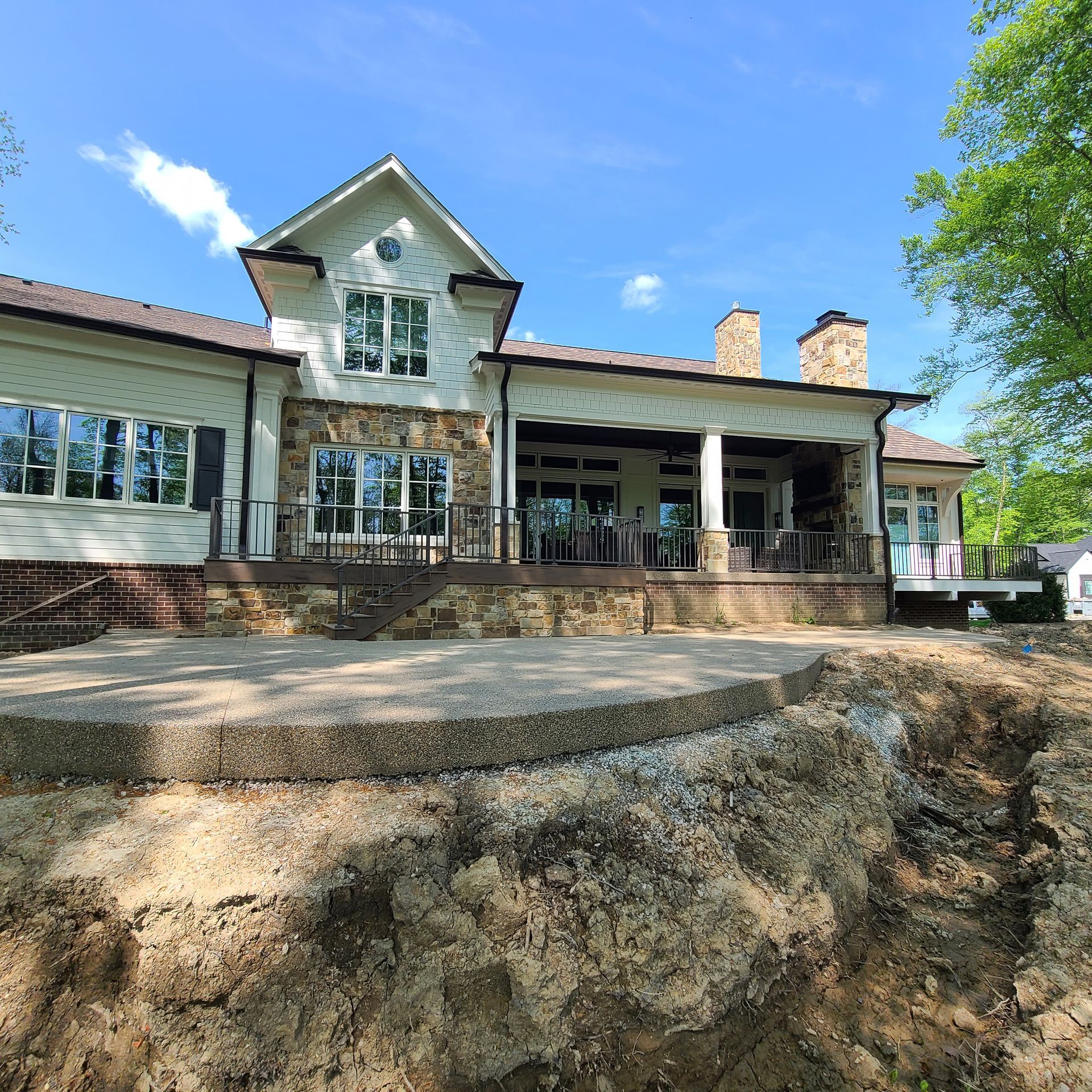Stone house with a covered porch and large windows, seen from a rocky foreground under a blue sky.
