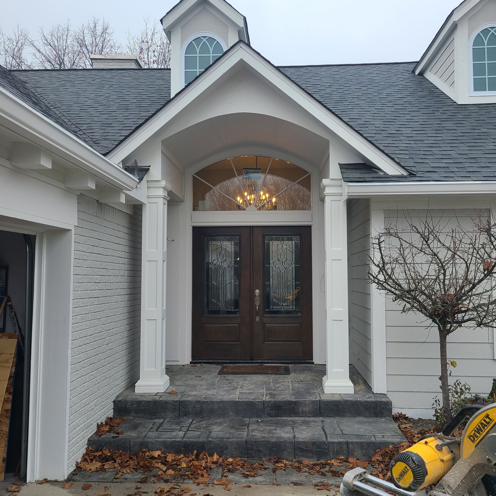 Front entrance of a house with white columns, dark double doors, and stone steps with fallen leaves.