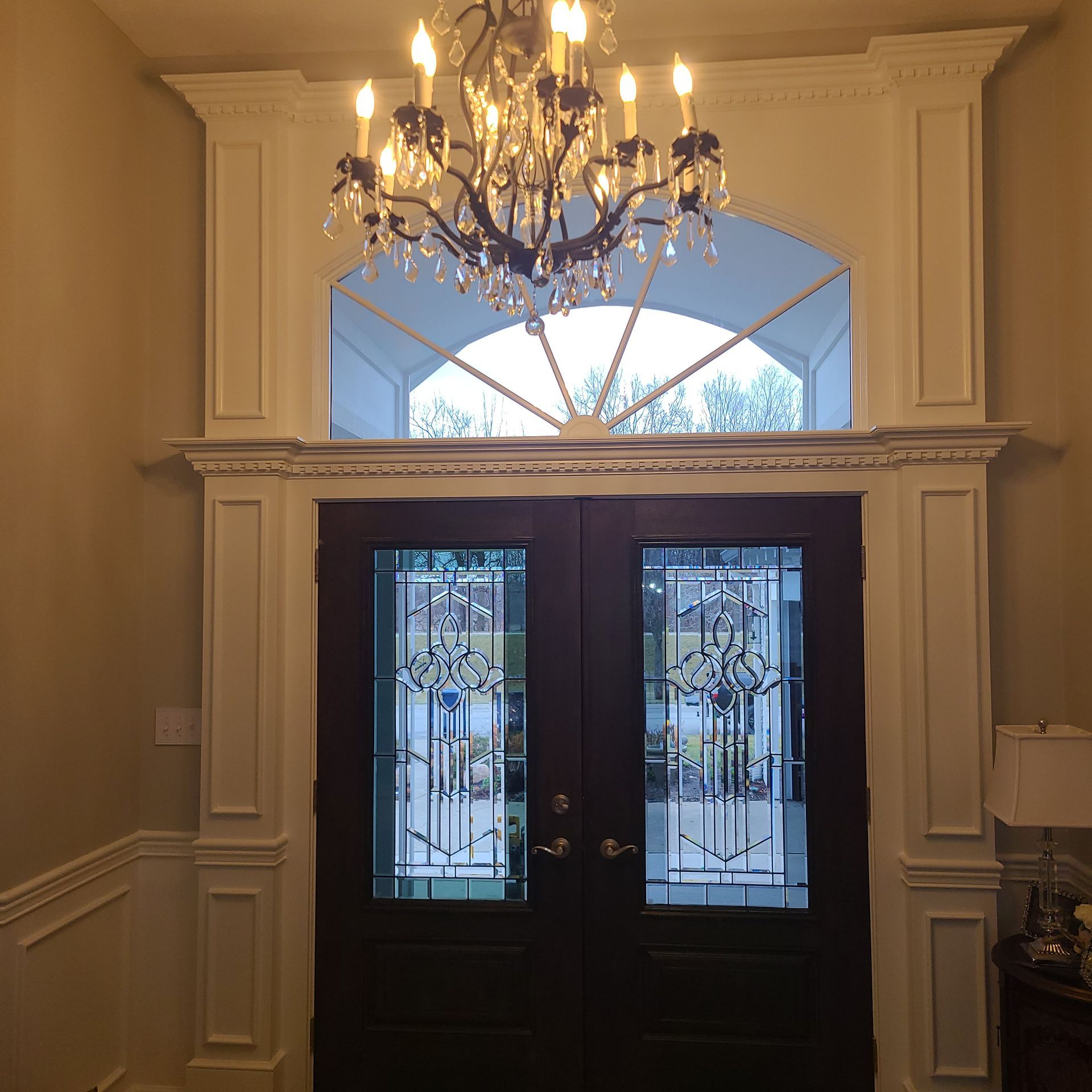 Elegant foyer with dark double doors, chandelier, and arched window above