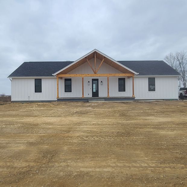 New white single-story house with a front porch and dark roof under an overcast sky