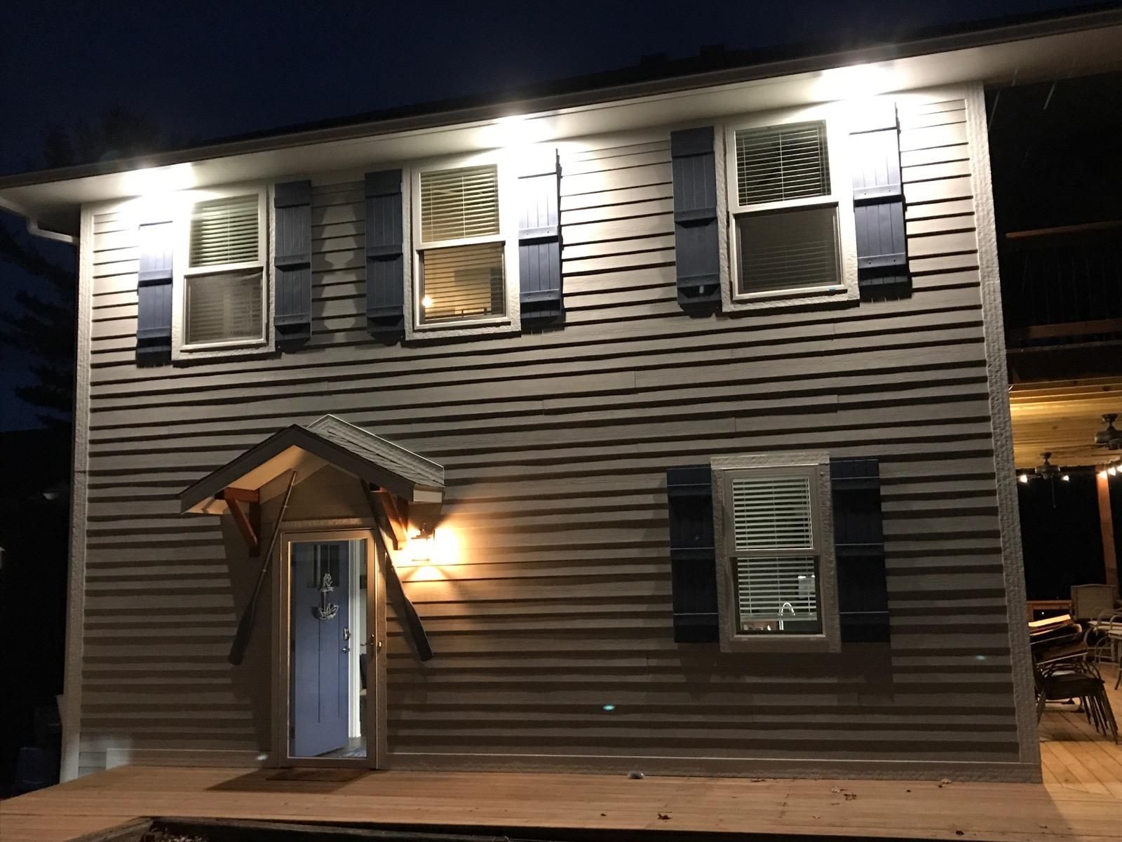 Two-story gray house at night with lit windows and a small front porch.