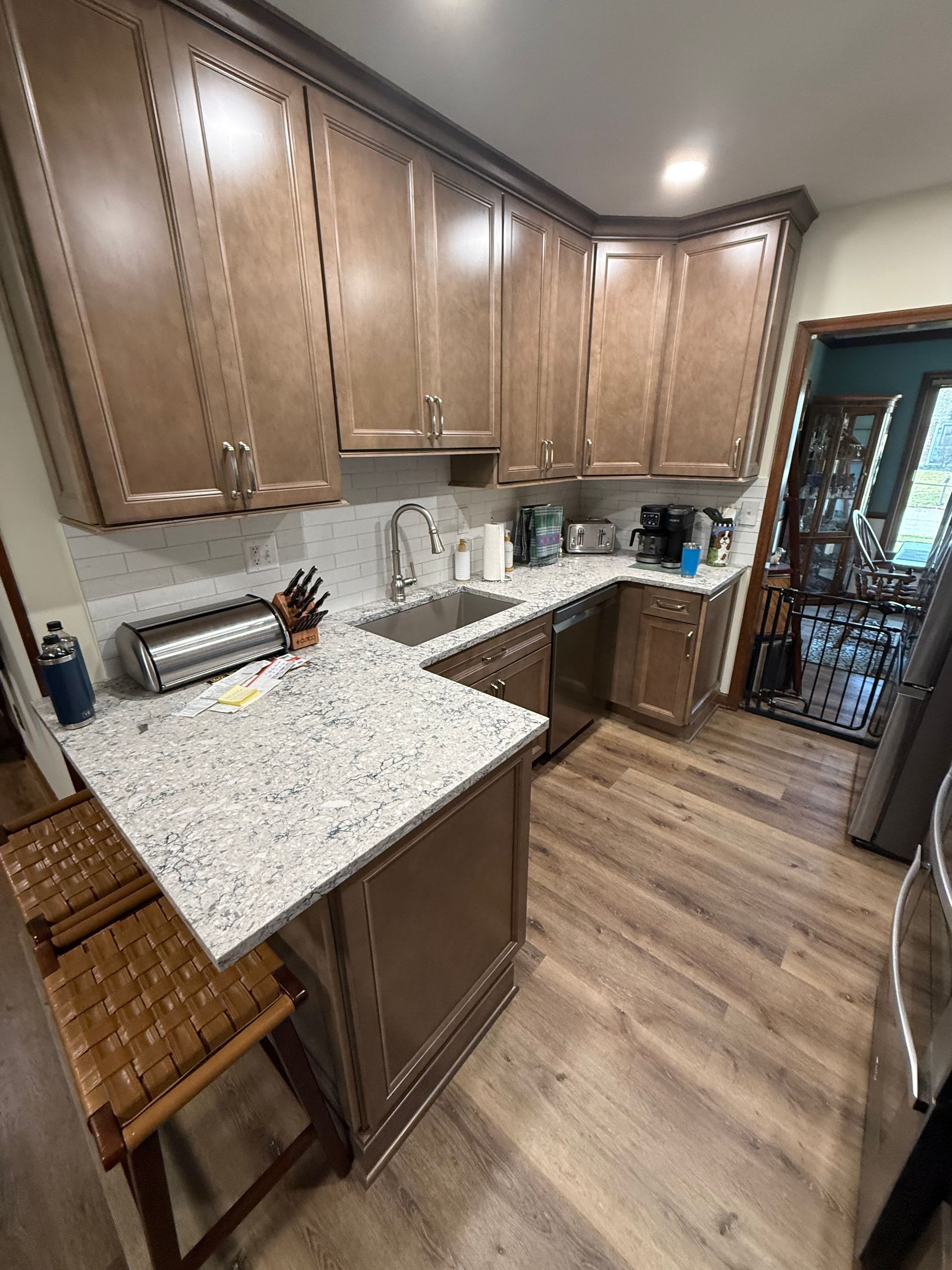 Modern kitchen with brown cabinets, speckled countertops, and wood-look flooring near a doorway.