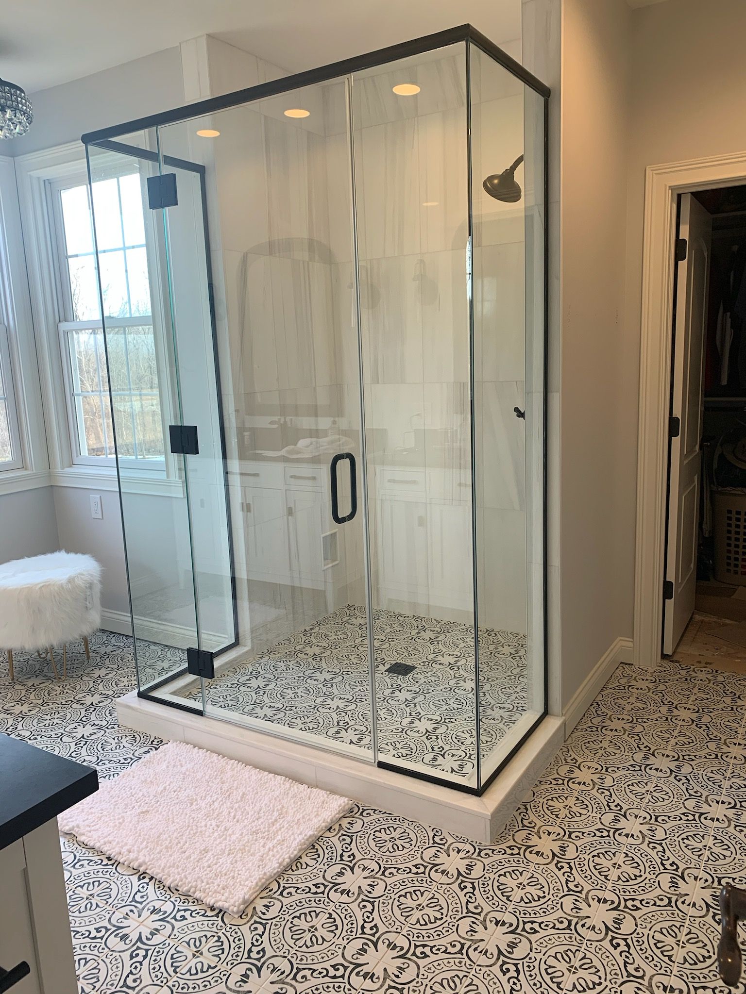 Modern bathroom with glass shower enclosure, patterned tile floor, and white vanity area