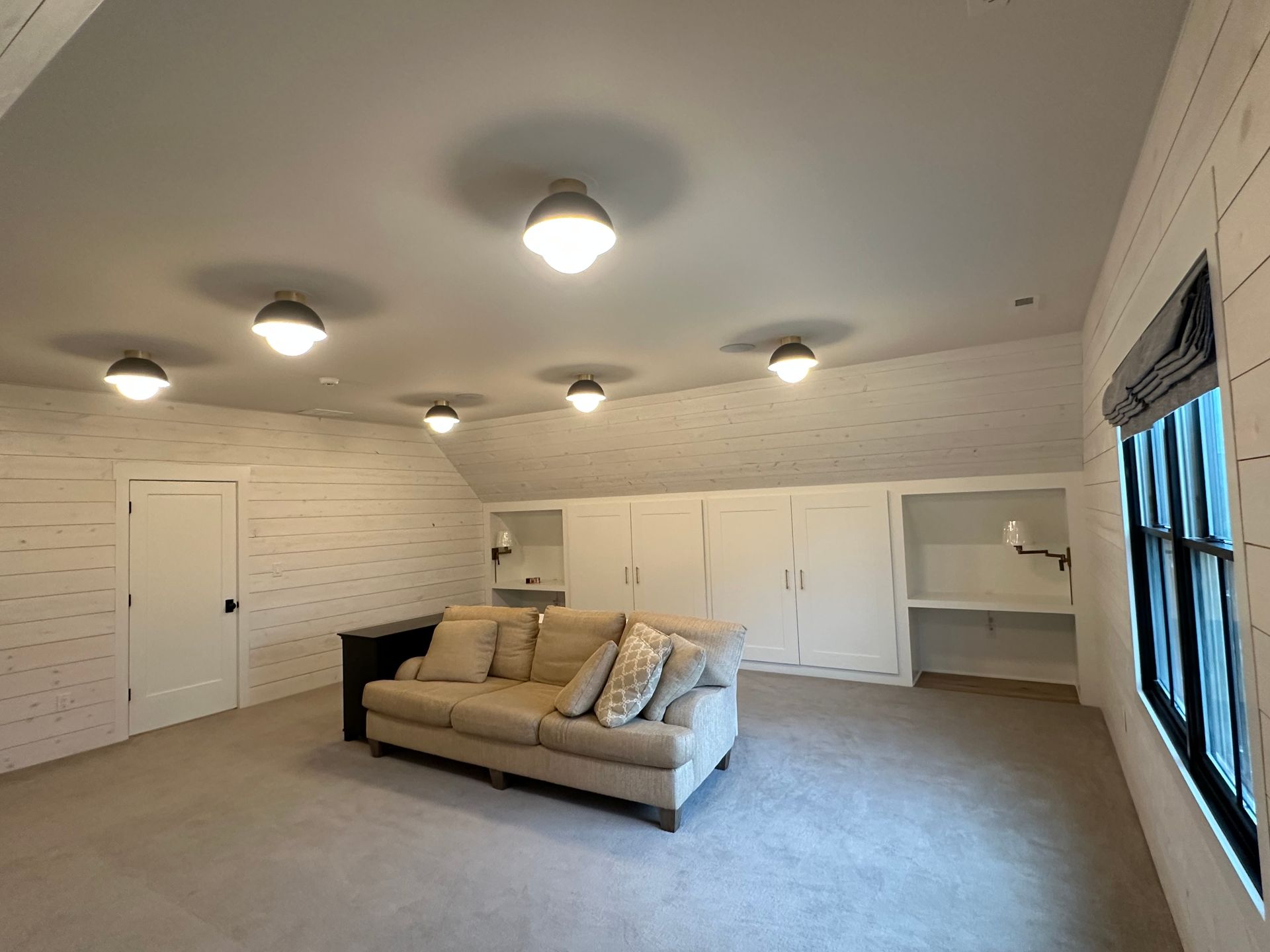 Spacious beige living room with sectional sofa, ceiling lights, and built-in storage along the wall