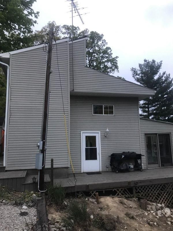 Gray two-story house with a tall chimney, deck, and utility pole on a rocky hillside.