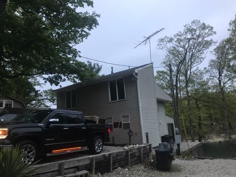 Black pickup truck parked beside a house with floodwater around the yard and road.