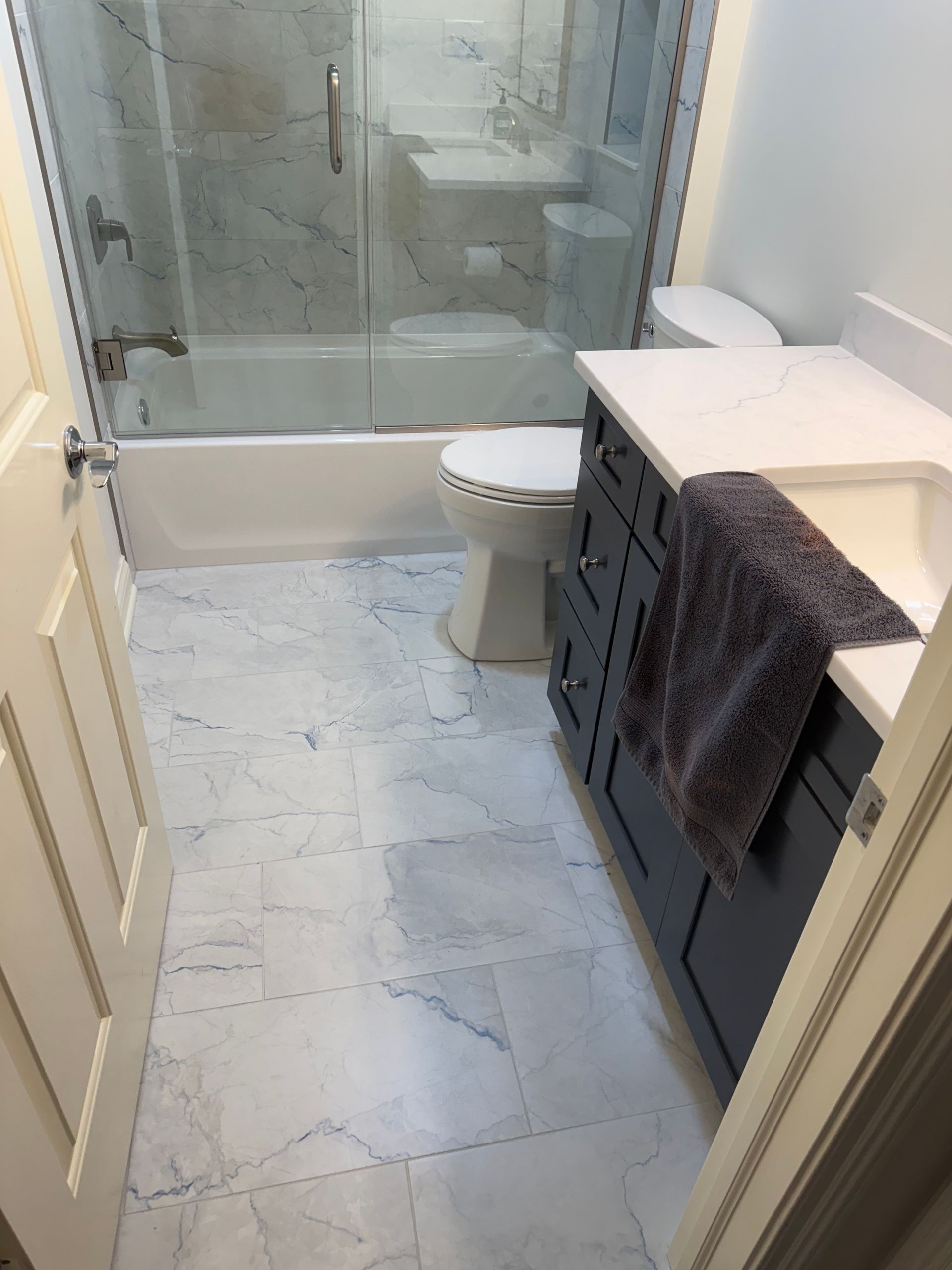 Small bathroom with glass shower, white vanity, toilet, and light marble tile floor.