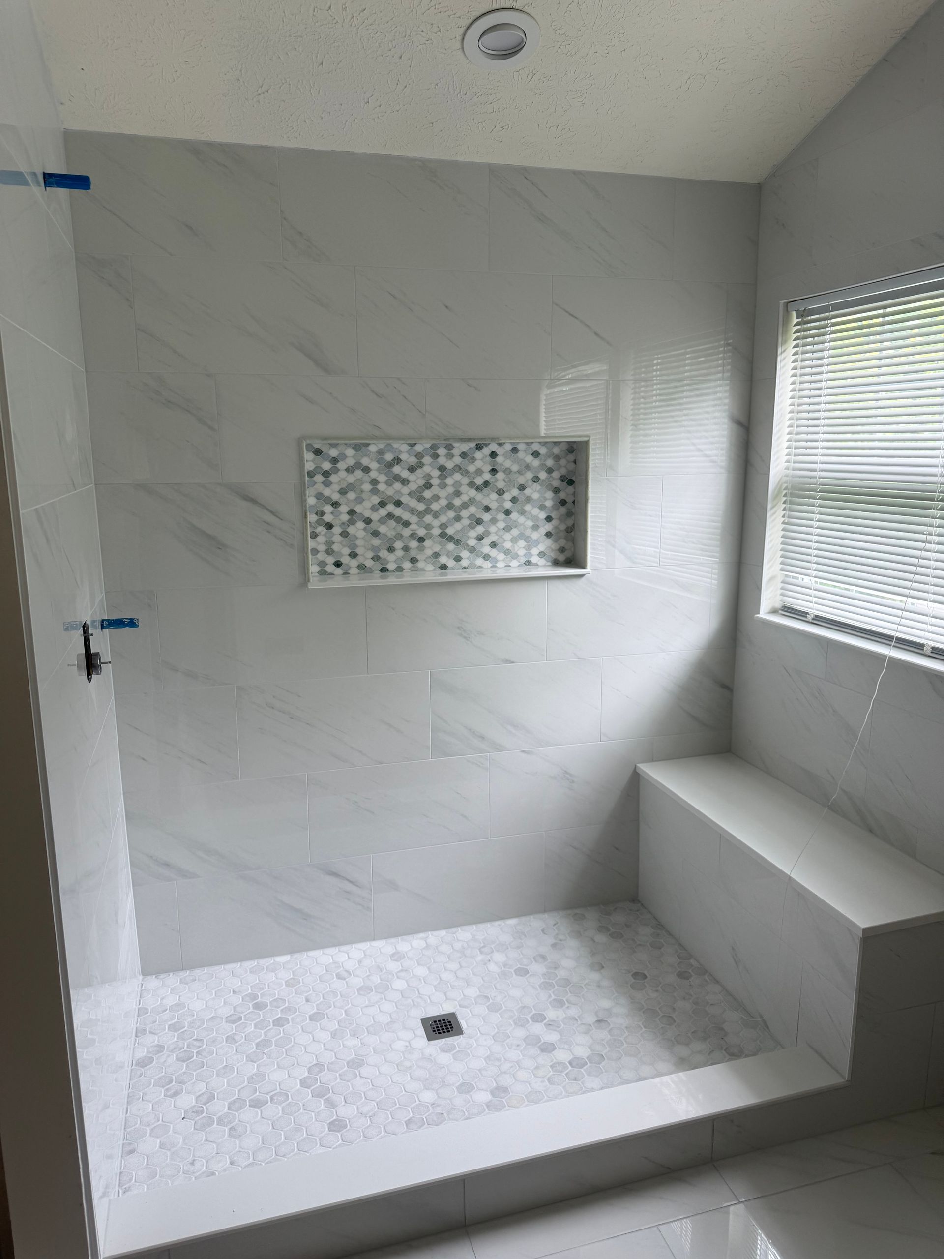 Empty white tiled shower with built-in bench, niche, and small window.