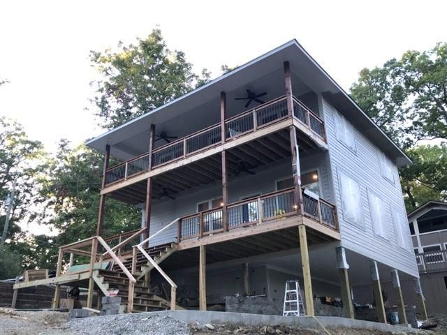 Raised gray house with wraparound porches and exterior stairs on stilts in a wooded area