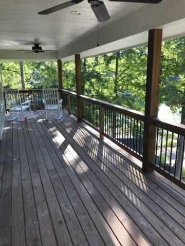 Covered wooden porch with railing, ceiling fans, and sunlit trees beyond