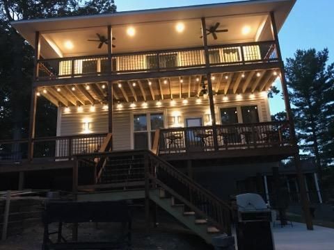 Two-story wooden cabin deck lit warmly at dusk, with stairs leading up to a porch.