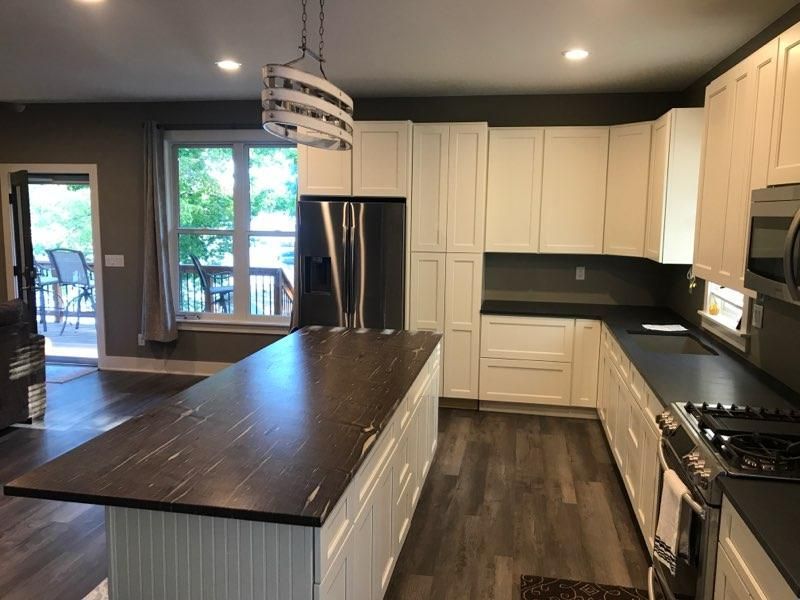 Modern kitchen with dark island, white cabinets, stainless appliances, and large windows.