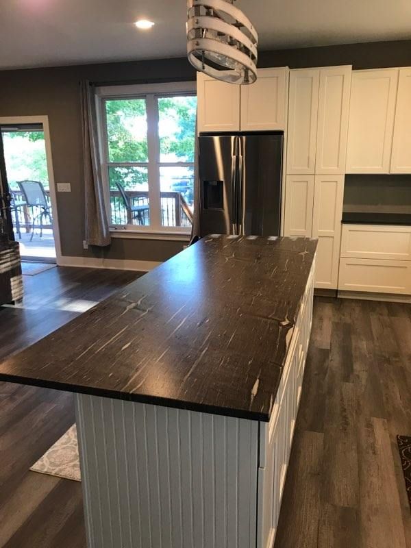 Modern kitchen with dark island countertop, stainless fridge, white cabinets, and wood-look flooring