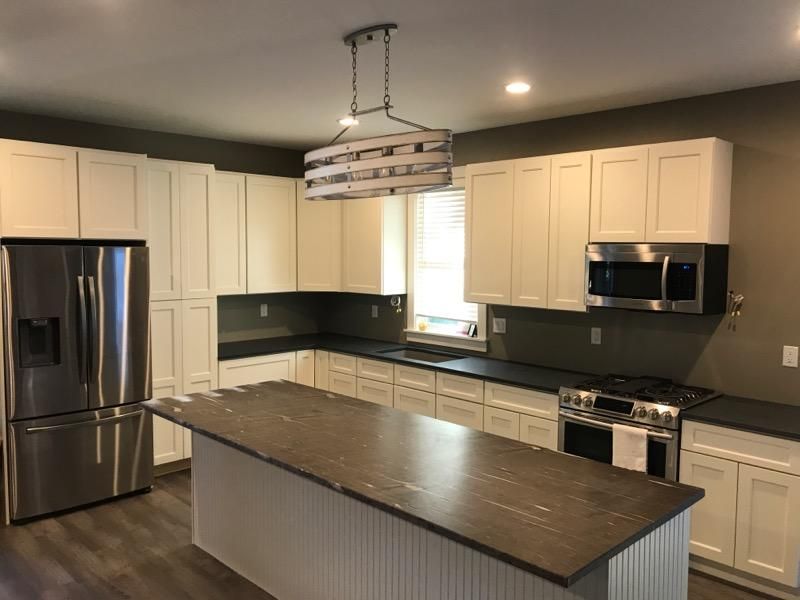 Modern kitchen with white cabinets, stainless appliances, dark countertops, and a large island under a pendant light