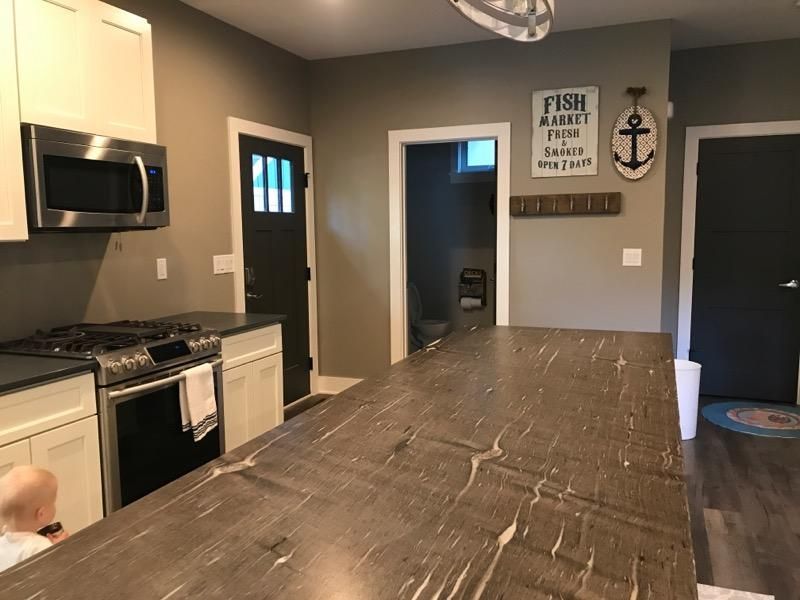 Modern kitchen with a large island, stainless appliances, and dark doors leading to a hallway
